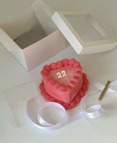 a pink heart shaped cake sitting on top of a table next to two white boxes