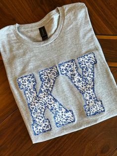 a t - shirt with the letters k and y printed on it sitting on a wooden floor