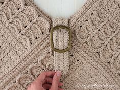 a person is holding onto a crocheted sweater with a metal ring on it