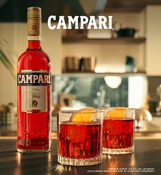 two glasses filled with red liquid next to a bottle of campari wine on a kitchen counter