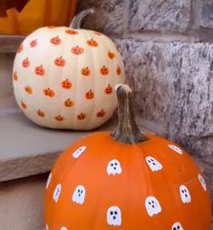 two pumpkins with ghost faces painted on them sitting next to each other in front of a brick wall