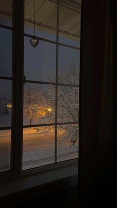 an open window in a dark room with snow on the ground and street lights outside