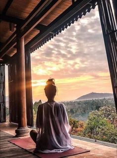 a woman sitting on top of a yoga mat in front of a window looking out at the mountains