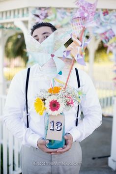 a man holding a jar with flowers and a number on it in front of a white fence