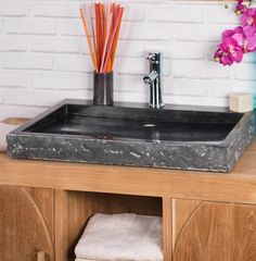 a bathroom sink sitting on top of a wooden counter next to a vase with flowers