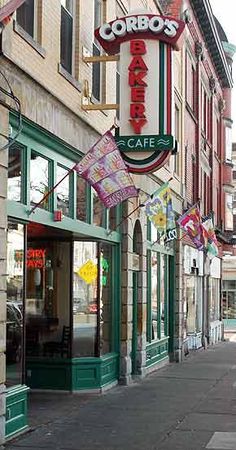 the corner of a city street with shops on both sides and signs hanging from buildings