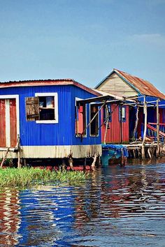 a blue house sitting on top of a body of water next to wooden poles and grass