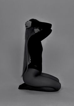 a woman with long hair sitting on the floor in tights and heels, posing for a black and white photo