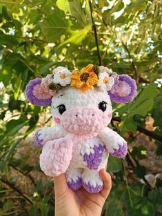 a crocheted stuffed animal with flowers on its head is held in front of some leaves