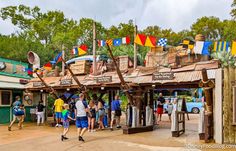 several people are walking around in front of an amusement park entrance with flags on it