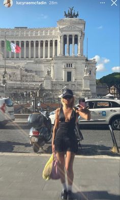 a woman standing in front of a building with cars and motorcycles behind her on the street