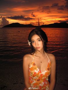 a beautiful young woman standing on top of a beach next to the ocean at sunset