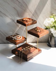 three tiered wooden trays with jewelry on them in front of a marble wall