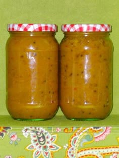 two jars filled with peanut butter sitting on top of a green tablecloth covered surface