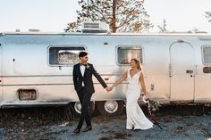 a bride and groom holding hands in front of an airstream