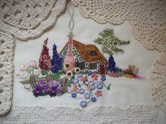 a white table cloth with a house and flowers on it, next to crocheted doily