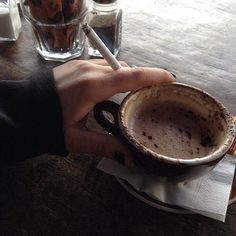 a person holding a coffee cup on top of a wooden table next to two glasses