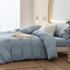 a bed with blue sheets and pillows in a bedroom next to a plant on the floor