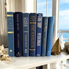 four blue books are sitting on a white shelf next to a window with the ocean in the background