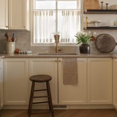 a kitchen with white cabinets and wooden stools in front of the window, next to an open sink