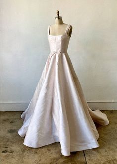 a white wedding dress on a mannequin in front of a wall with a vase