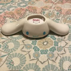 an elephant shaped bowl sitting on top of a flowery tablecloth with a sticker in it's mouth