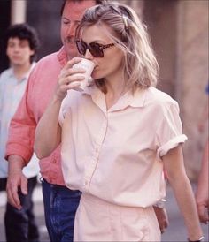 a woman is walking down the street while holding a cup in her hand and drinking from a paper cup