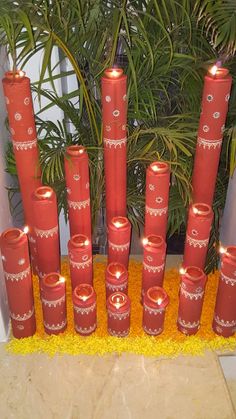 many red candles are lit in front of a plant with yellow flowers on the ground