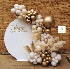 a balloon arch with gold and white balloons on it in front of a brick wall