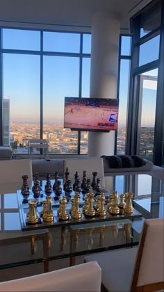 a glass table with chess pieces on it in front of large windows overlooking the city