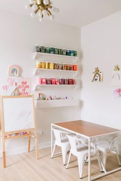 a table and chairs in a room with shelves on the wall above it, and an easel next to them