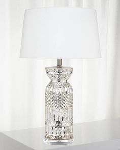 a clear glass table lamp with a white shade on the top and bottom part of it