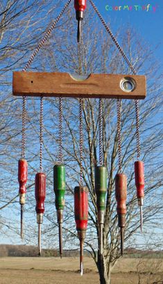 a wind chime hanging from a tree in the middle of a field with lots of red, green and blue tin canisters attached to it