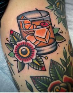 a close up of a person's leg with tattoos on it and an orange drink