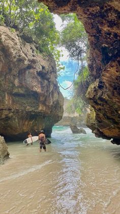 two people carrying surfboards into the water through some large rock formations in the ocean