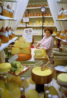 a woman standing behind a counter filled with cheese