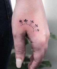 a woman's left hand with small black flowers on the middle finger and dots in the middle