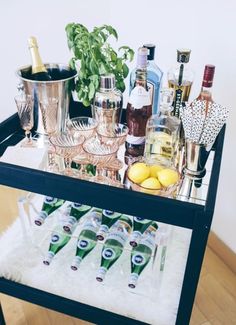 a bar cart filled with liquor bottles and glasses on top of a wooden floor next to a potted plant