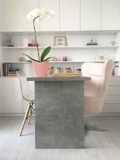 a chair and table in a room with white cabinets, pink flowers and bookshelves