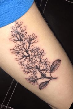 a black and white photo of a branch with flowers on the side of a woman's leg