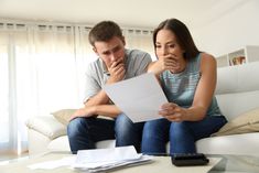 a man and woman sitting on a couch looking at paperwork