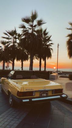 an old yellow car parked on the side of the road next to some palm trees