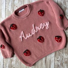 a pink sweater with ladybugs on it and the word's name written in cursive writing