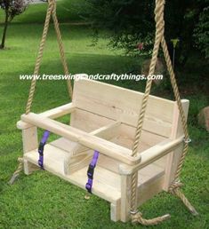 a wooden swing with rope hanging from it's sides on the grass in front of some trees