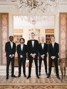 a group of men in tuxedos standing next to each other near a chandelier