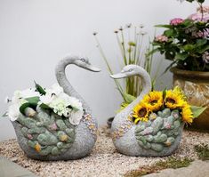 two statues of swans with flowers in their beaks, sitting on the ground next to each other