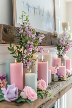 pink and purple flowers are arranged on a mantel with candles in front of it