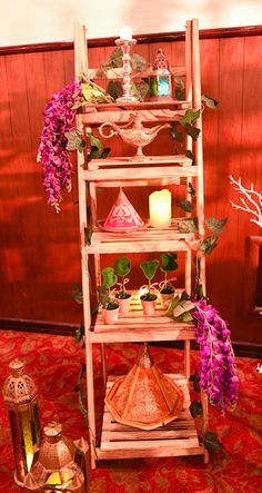 a tall wooden shelf with candles and flowers on top of it in front of a red wall