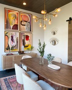 a dining room table with white chairs and paintings on the wall