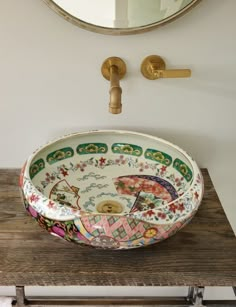 a bowl shaped sink sitting on top of a wooden counter next to a round mirror